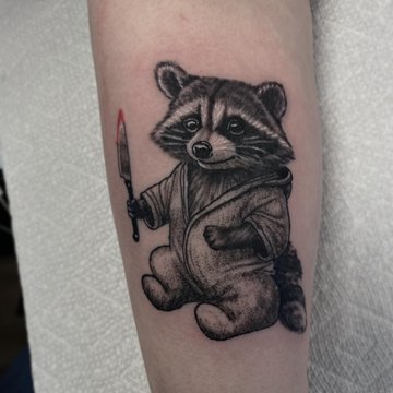 Tatouage de raton laveur en noir et gris, style dessin animé, en combinaison, tenant un couteau à lame rouge, symbolisant ruse, ingéniosité et esprit joueur.